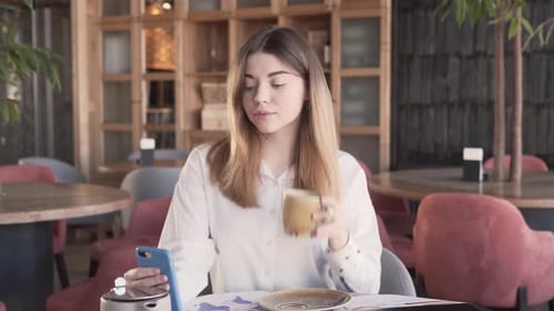 Woman Using Phone and Drinking Coffee at Cafe