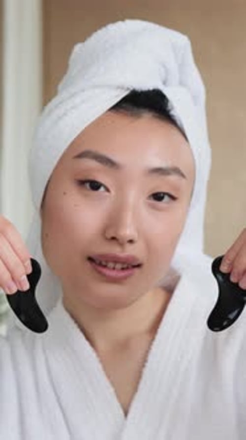 Woman in bathrobe with towel showing facial tools