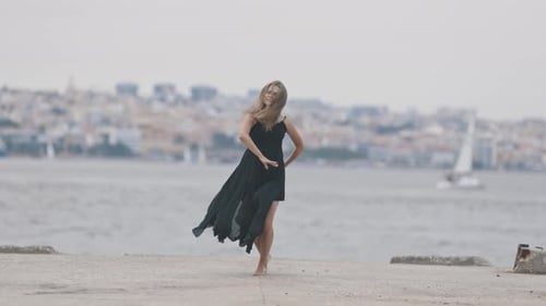 An Adult Smiling Woman in Black Dress Dancing on the Pier European Town