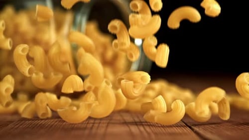 Elbow pasta flying from glass jar on wood