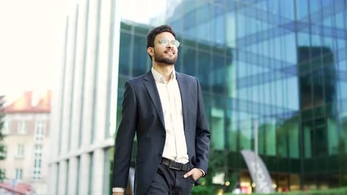 Confident businessman in a suit walks down street near an office building. Successful bearded