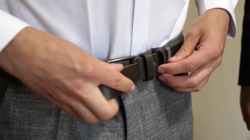 19 1A man fastens his belt on his pants. Stylish men's clothing.