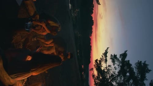 Hipster Man and a Young Beautiful Girl Prepare a Picnic Lunch While Friends Play Ball Near a Pine