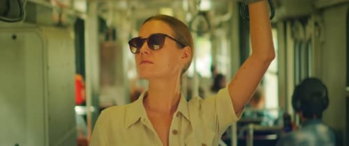 Femme debout dans le transport en commun tenant une sangle tout en portant des lunettes de soleil