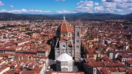 Aerial view of Cathedral of Santa Maria del Fiore zooming out with city and mounatins on a sunny day