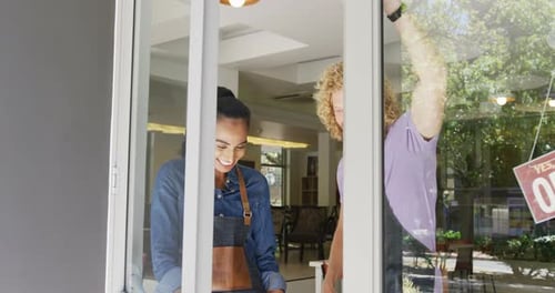 Portrait of happy diverse male and female baristas standing in doorway of their coffee shop