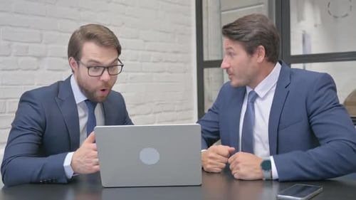 Businessmen Celebrating Success at Office Desk with Laptop