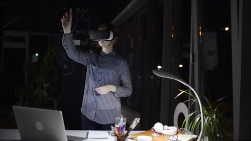 Tired businesswoman wearing vr goggles reaching out in a dark office at night