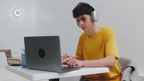 Student Focused on Studying in a Cozy Room with a Laptop Notebook and Headphones During Late