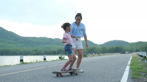 Mother teaching her daughter how to skateboard in the park. Child riding skate board.