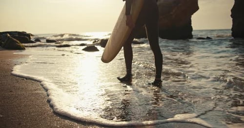 Surfer Walking on Beach with Surfboard at Sunset