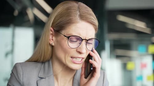 Angry businesswoman in a suit arguing talking on mobile phone at workplace in business office.