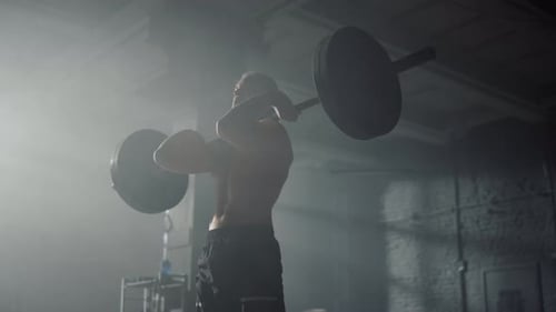 Strong Sportsman Standing with Barbell on Shoulders in Fitness Gym. Shirtless Man