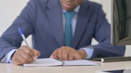 Close Up of Young African Businessman Writing on Notebook