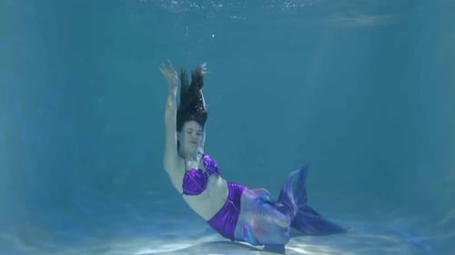 Elegante hübsche Meerjungfrau mit langen Haaren, die anmutig unter Wasser schwimmt