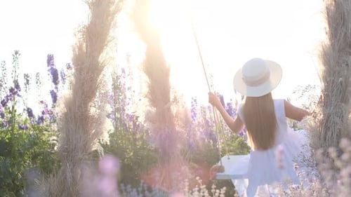A Young Lady in a White Style is Swinging on a Beautiful Swing in the Middle of a Field