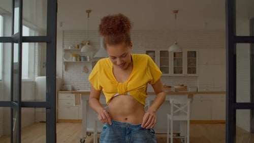 Excited Pretty African Female in Too Large Jeans Showing Weight Loss Success