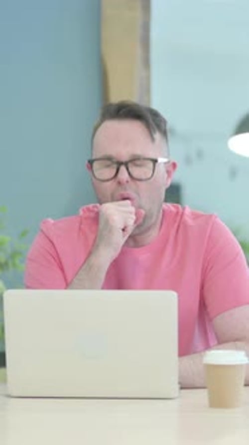 Man in glasses coughing while working on laptop