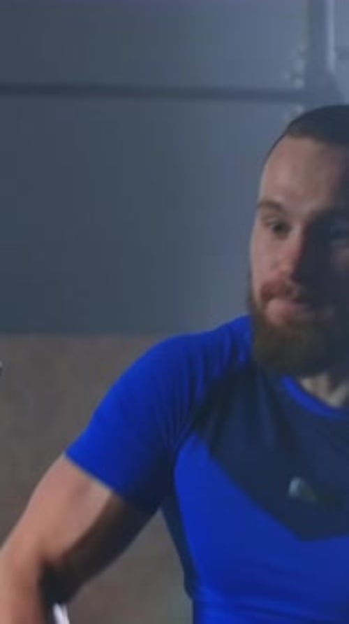 Athletic Man in Blue Sportswear Performing Intense Upper Body Exercise on Gym Equipment in a Dimly