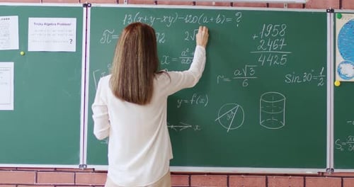 Back View of Female Teacher Standing Near Green Chalkboard and Writing Geometric Formula in