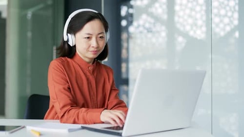 Mujer asiática con auriculares inalámbricos, programadora profesional de TI que trabaja escribiendo y codificando en una computadora portátil mientras