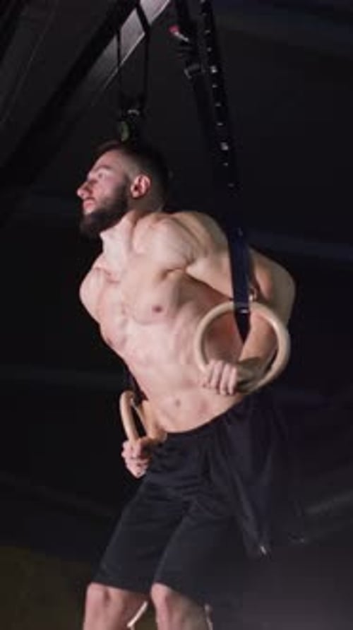 Vertical Video Male Gymnast is Working Out on a Rings in the Dark Gym