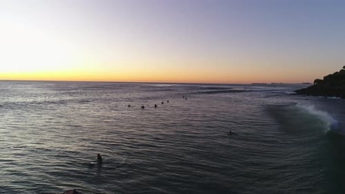 Aerial silhouette pull away following a group of surfers paddling out waiting for the right wave dur