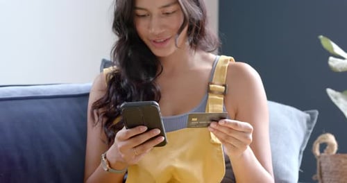 Woman Using Phone and Credit Card on Couch