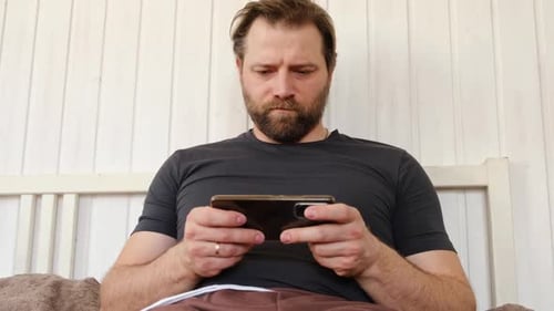 Man Sitting on Bed Using Mobile Phone