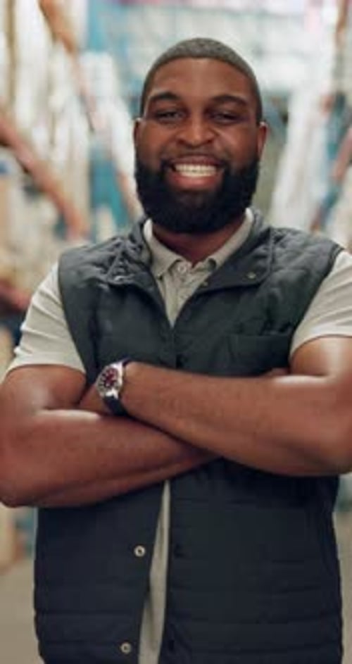 Bearded Man Smiles With Arms Crossed in Warehouse