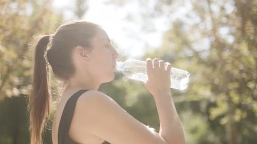 Young White Woman Drinks Water From a Bottle After Fitness Training Outdoors in the Park