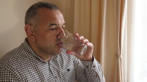 1. Ein Mann trinkt Wasser aus einem Glas, während er am Tisch sitzt.