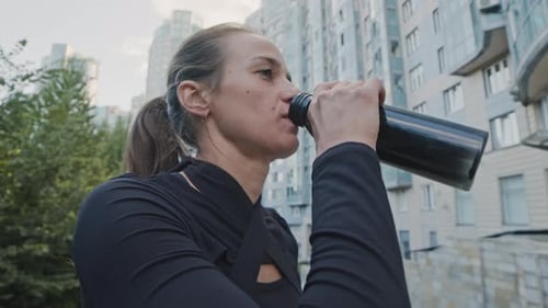 Woman Drinks Water in an Urban Setting