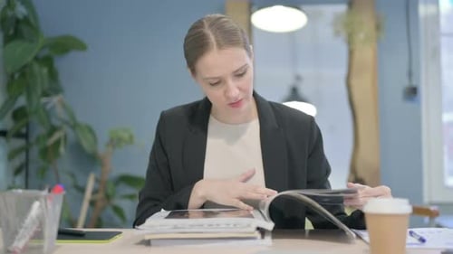 Young Adult Woman Reads a Magazine at Her Desk