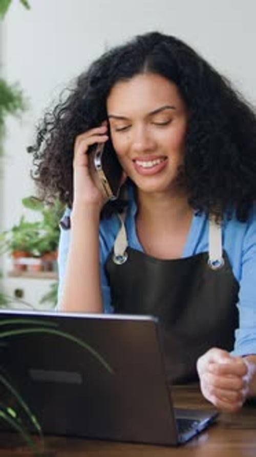 Portrait of African American Businesswoman in an Apron Sitting in Own Flower Store and Talking on a