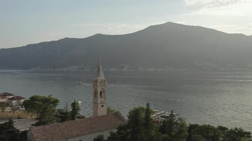 Drone parallax shot around the spire of the Church of Saint Eustace with a view of the bay in Kotor