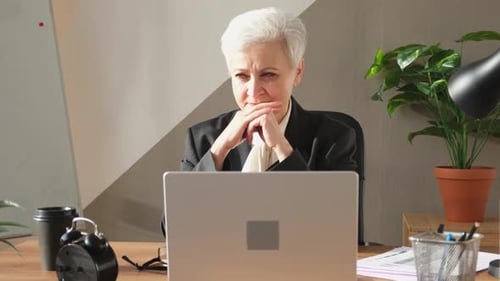 Thoughtful Mature Woman Working at Desk with Laptop