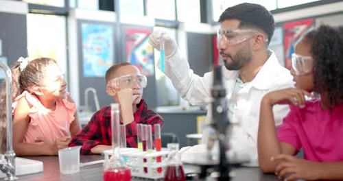 In a school classroom, a biracial teacher demonstrates a chemistry experiment