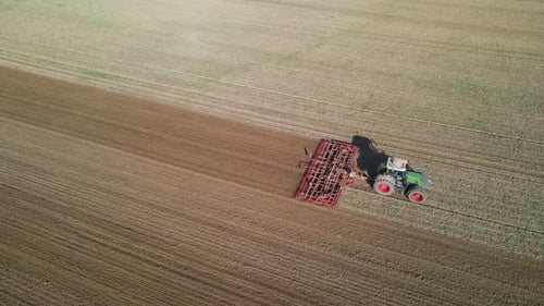 An aerial footage of a tractor working on a large agricultural field on a sunny day.