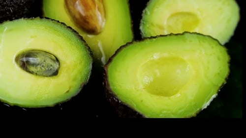 Drops of water fall on avocado fruits with leaves on a black background. Raw Fruits, healthy food.
