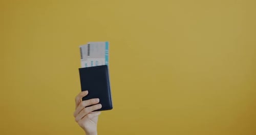 Hand Raising Passport with Tickets and Toy Plane on Yellow Background