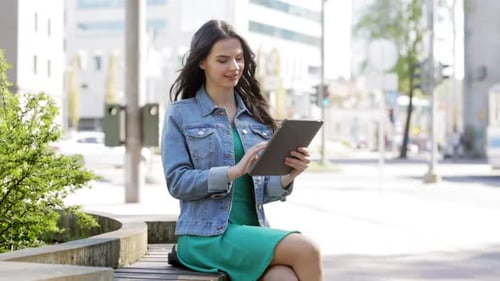 Woman Using Tablet Device Sitting on Bench in City