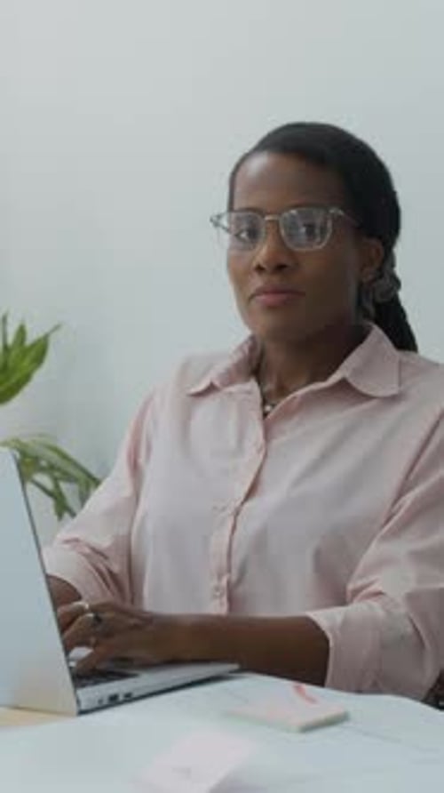 Cheerful Black Female Employee Working in Laptop at Office Desk, Vertical