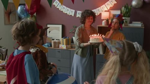 Woman Holding Lit Cake for Child to Blow Out Candles During Birthday Celebration