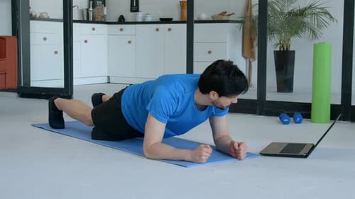 Sporty Fit Man Watching Tutorial Video on Laptop Doing Yoga Plank