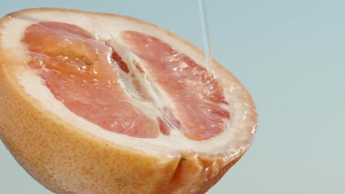 Half of a red grapefruit, water dripping from it, against the blue sky. Slow mo, close up
