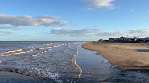 Warm coastal sunset scene with people walking through the image. Warm tones with gentle waves and st