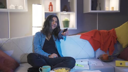 Man Eating Food on Sofa Watches Television