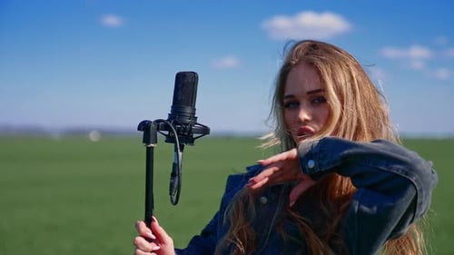 Beautiful girl singer in a green field. Attractive blond woman singing into a microphone