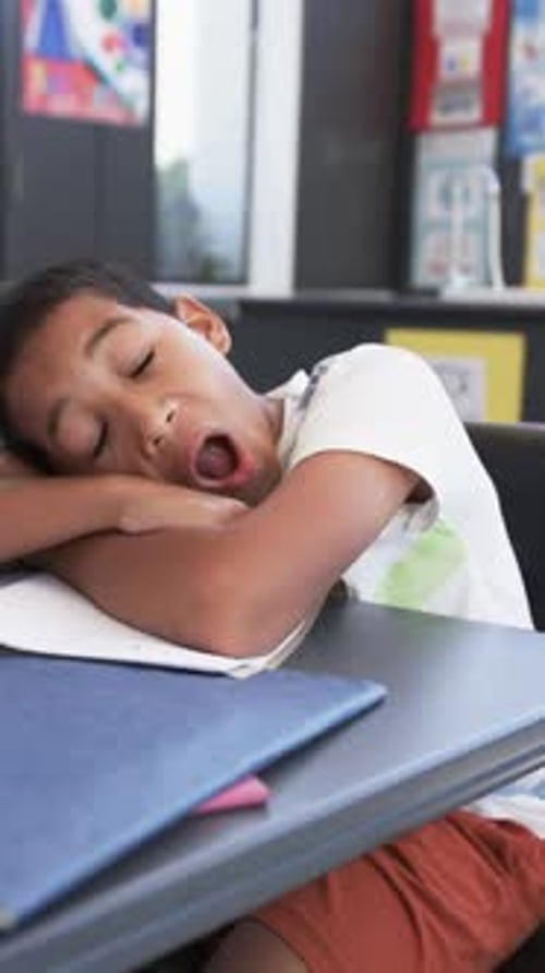 Vertical video: In school, child sleeping on desk with open notebook, feeling tired